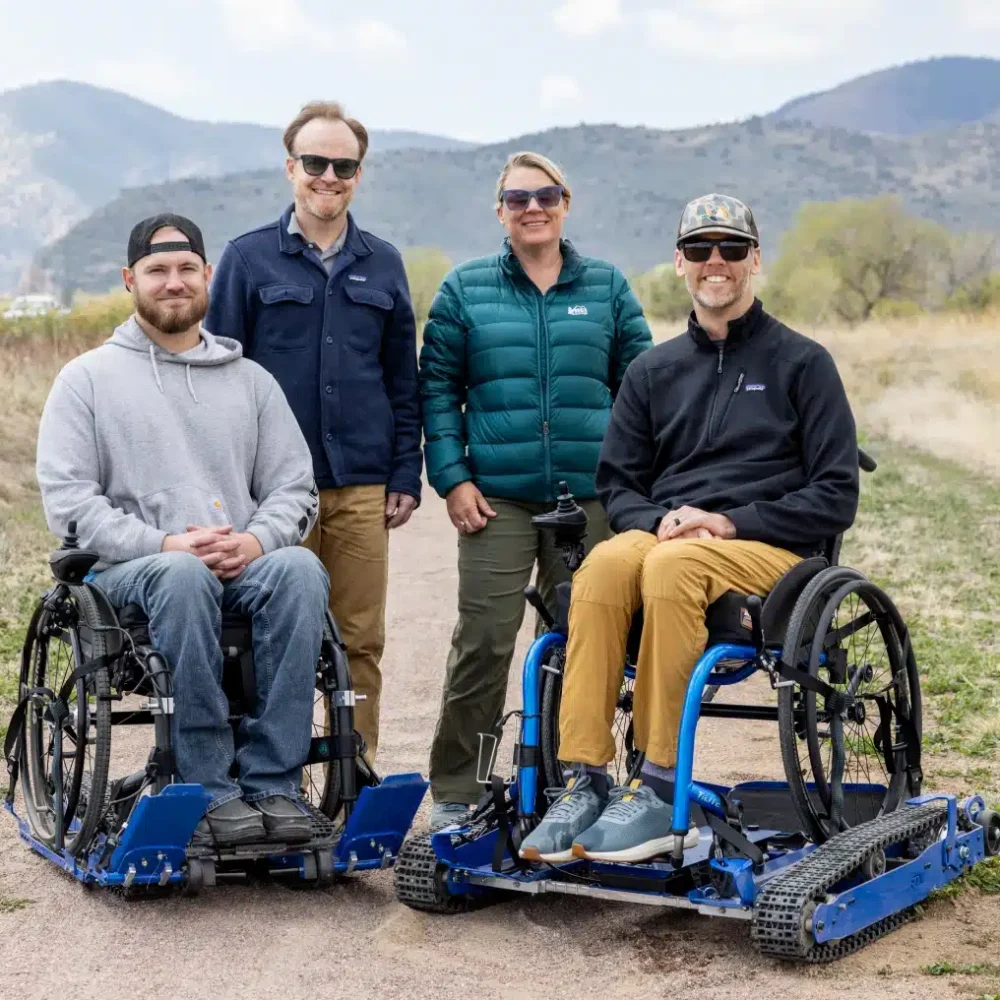 Two people in Freedom Trax wheelchairs and two people standing on outdoor trail